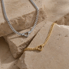 Chunky curb chain necklace with open heart pendant in gold and silver stainless steel on neutral background
