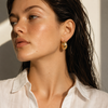 Gold and silver dome hoop earrings with a brushed texture and rounded sculptural shape, shown on a white background.