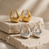 Gold and silver dome hoop earrings with a brushed texture and rounded sculptural shape, shown on a white background.