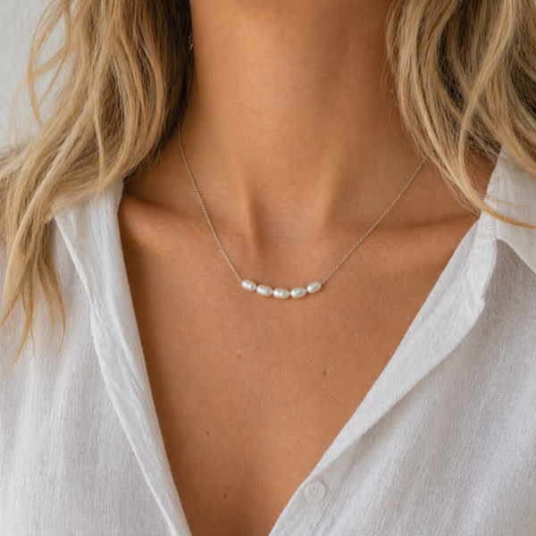 Lagoon pearl necklace with five organic pearls spaced along a fine stainless steel chain, available in gold and silver, worn at collarbone length.