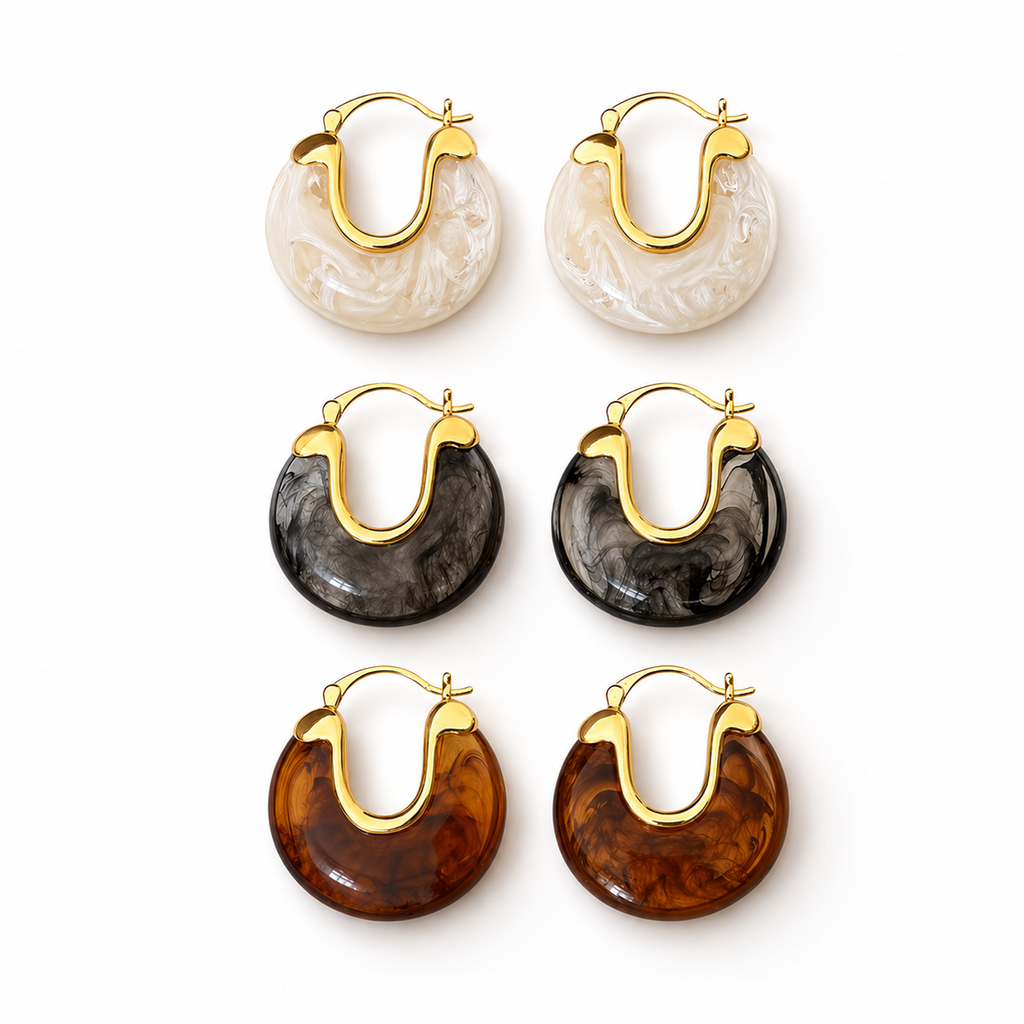 Gold hoop earrings with glossy marbled resin in pearl, smoke, and amber colour options on a white background.