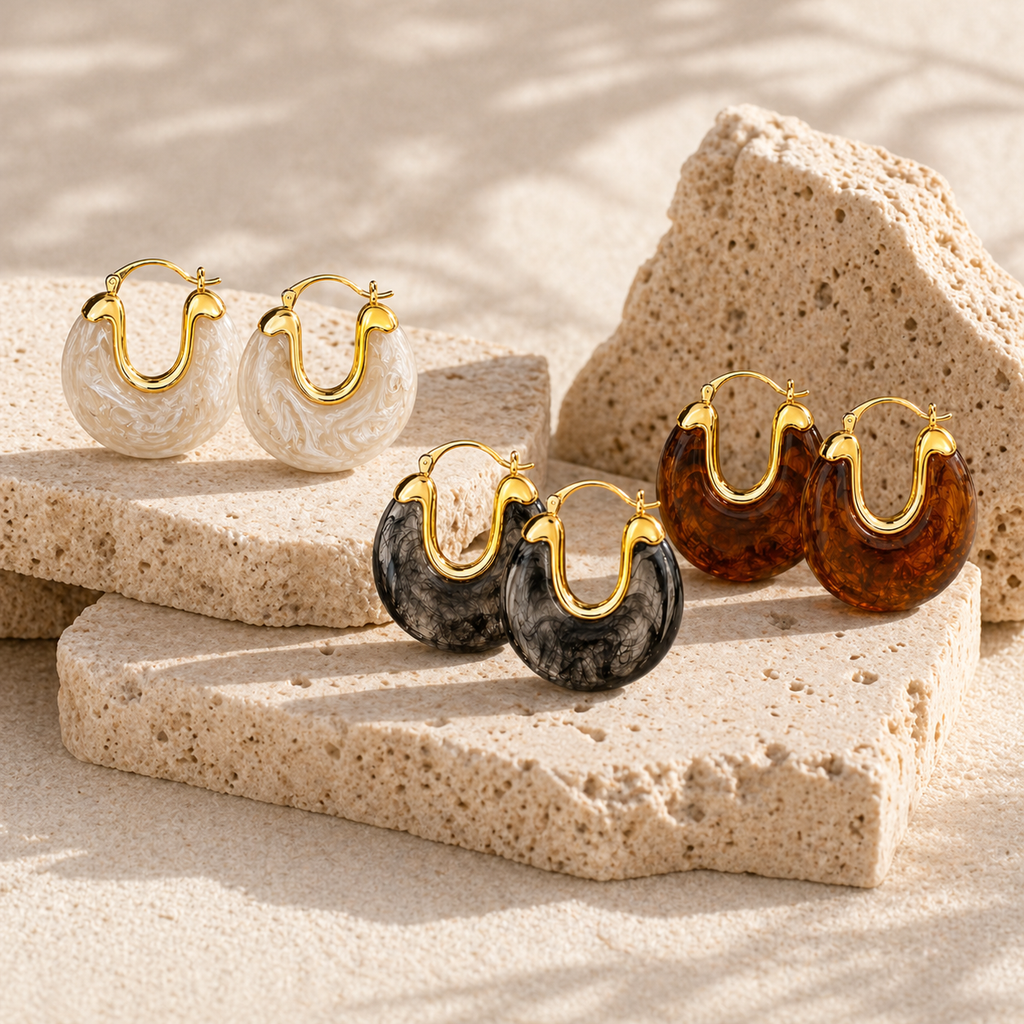 Gold hoop earrings with glossy marbled resin in pearl, smoke, and amber colour options on a white background.
