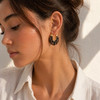 Gold hoop earrings with glossy marbled resin in pearl, smoke, and amber colour options on a white background.