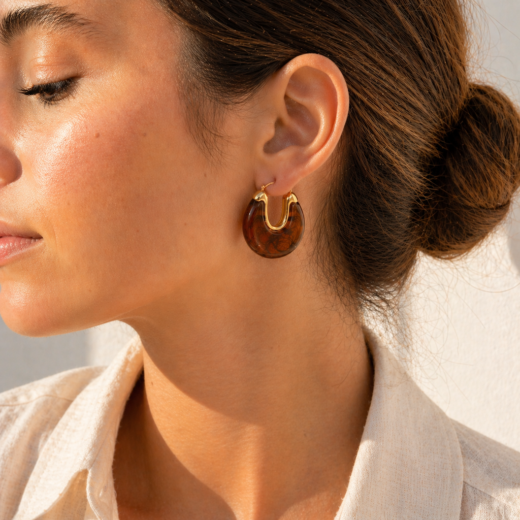 Gold hoop earrings with glossy marbled resin in pearl, smoke, and amber colour options on a white background.