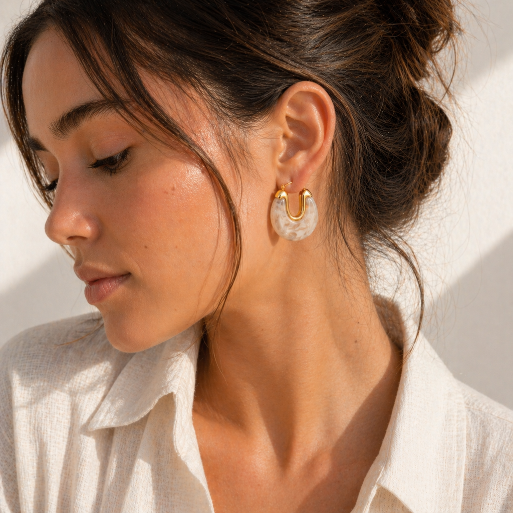 Gold hoop earrings with glossy marbled resin in pearl, smoke, and amber colour options on a white background.