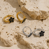 Gold and silver huggie earrings with black stone flower detail on a clean white background.