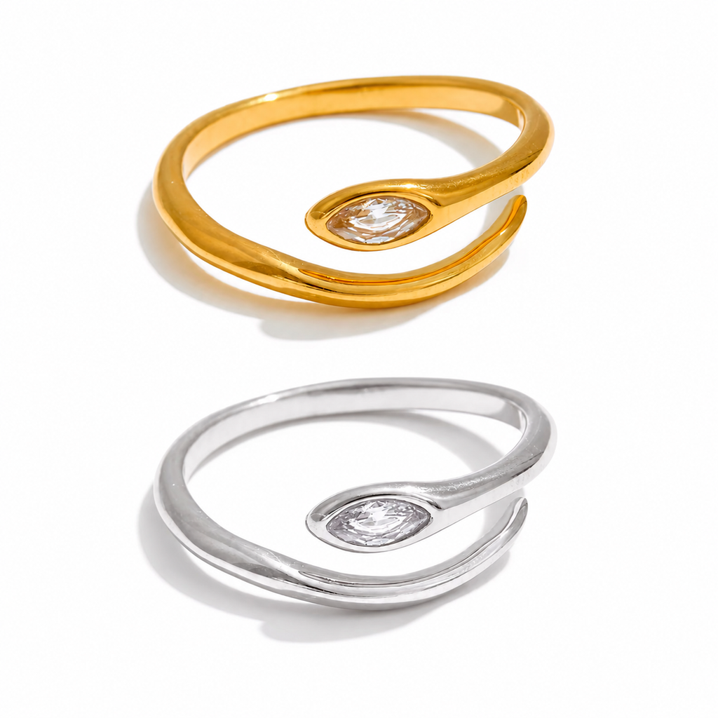 Gold and silver adjustable open-band rings with marquise crystal detail displayed on raw travertine stone.
