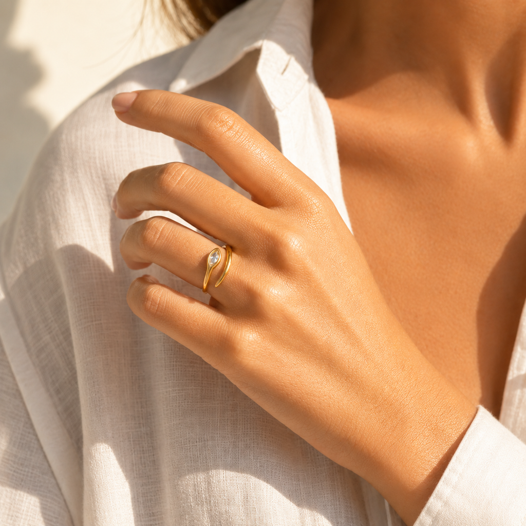 Gold and silver adjustable open-band rings with marquise crystal detail displayed on raw travertine stone.
