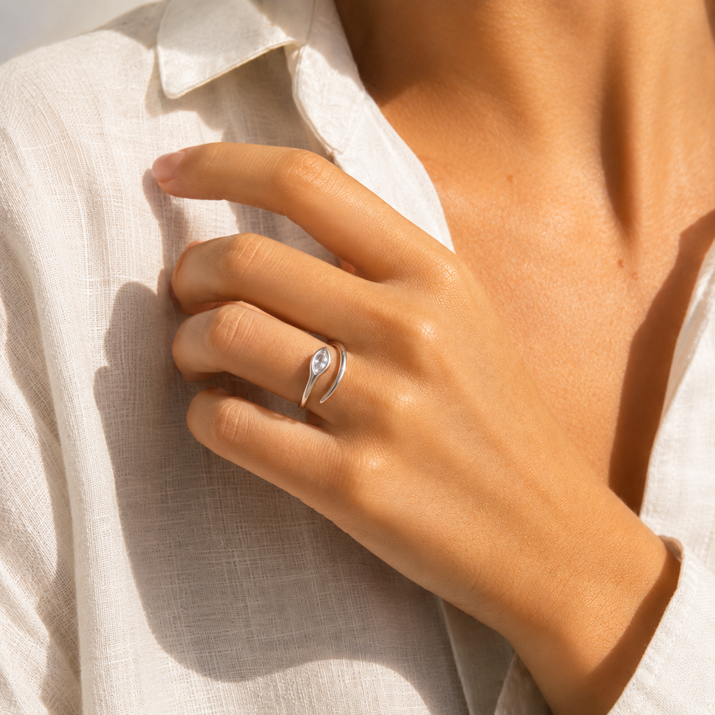 Gold and silver adjustable open-band rings with marquise crystal detail displayed on raw travertine stone.
