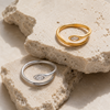 Gold and silver adjustable open-band rings with marquise crystal detail displayed on raw travertine stone.
