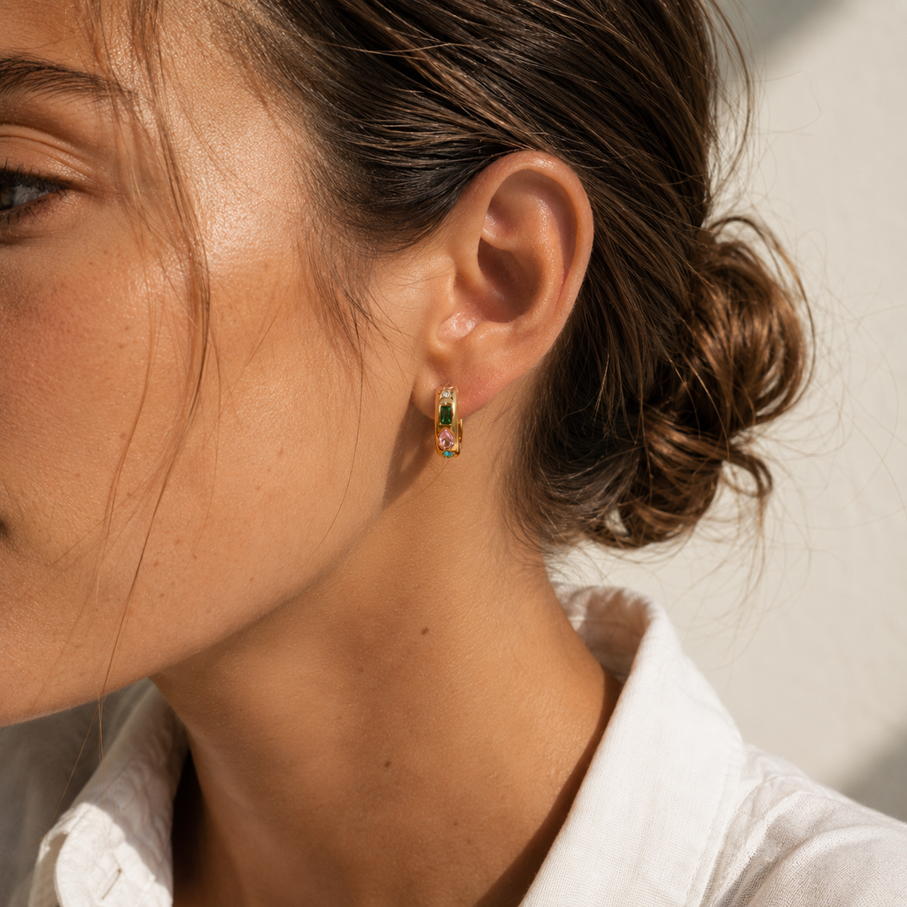 Gold and silver huggie earrings with colourful gemstone settings including green, pink, and blue stones with a star detail.